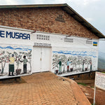 Mural en la fachada de la estación de lavado Musasa en Ruanda, con ilustraciones de caficultores recolectando cerezas. Edificio de ladrillo con certificaciones Fair Trade, Rainforest Alliance y prácticas sostenibles. Reflejo del trabajo comunitario detrás del café de especialidad que Artisan Coffee tuesta en Málaga para espresso y filtrado.