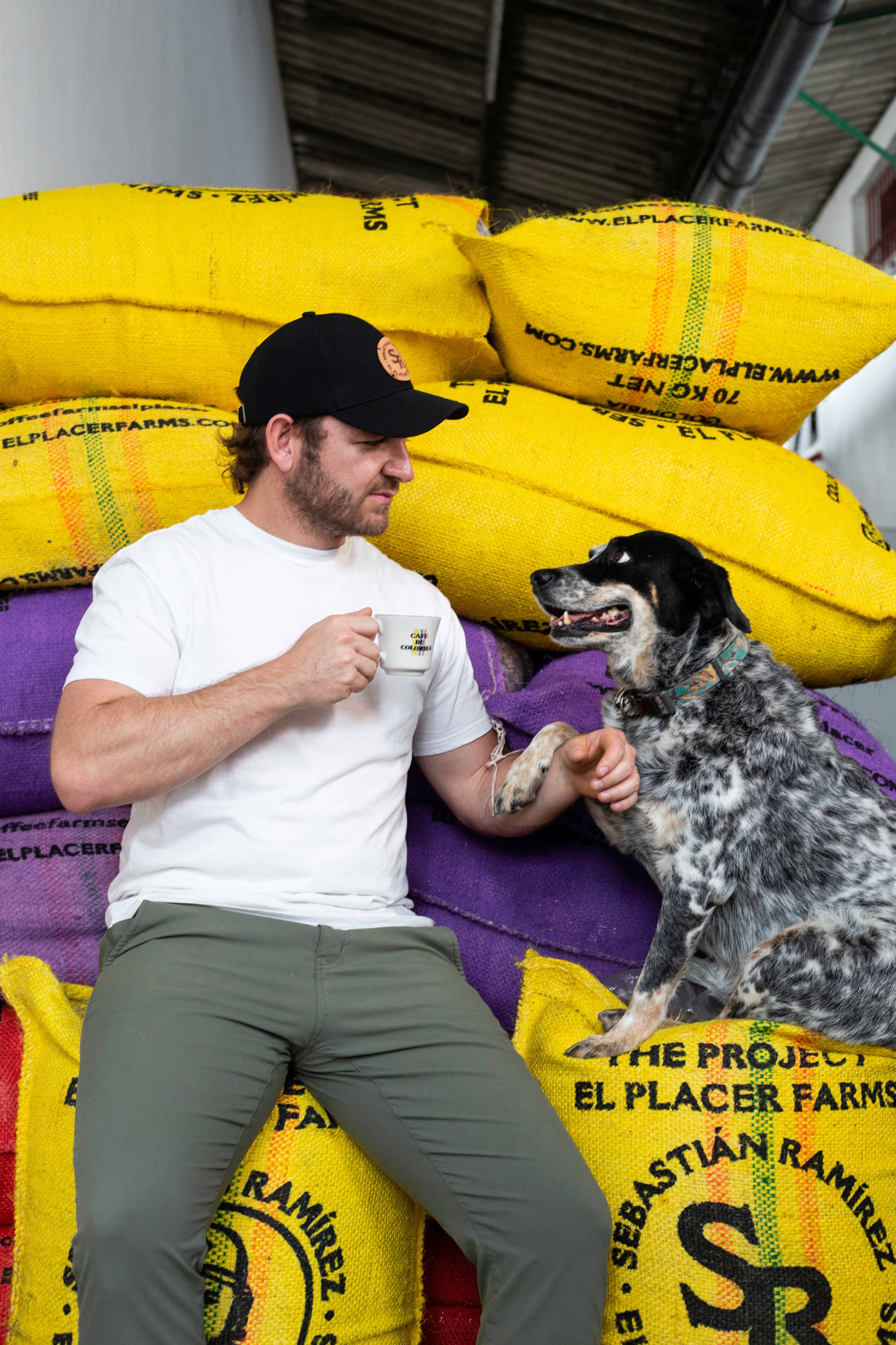 Sebastian Ramirez productor colombiano con su perro tomando una taza de café de especialidad sobre unos sacos de café de Colombia